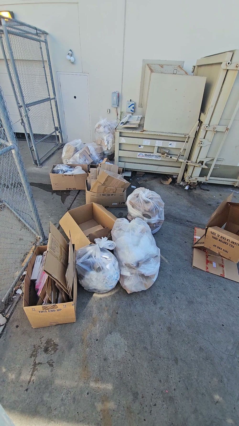 Trash bags and cardboard boxes piled near a commercial waste disposal area.