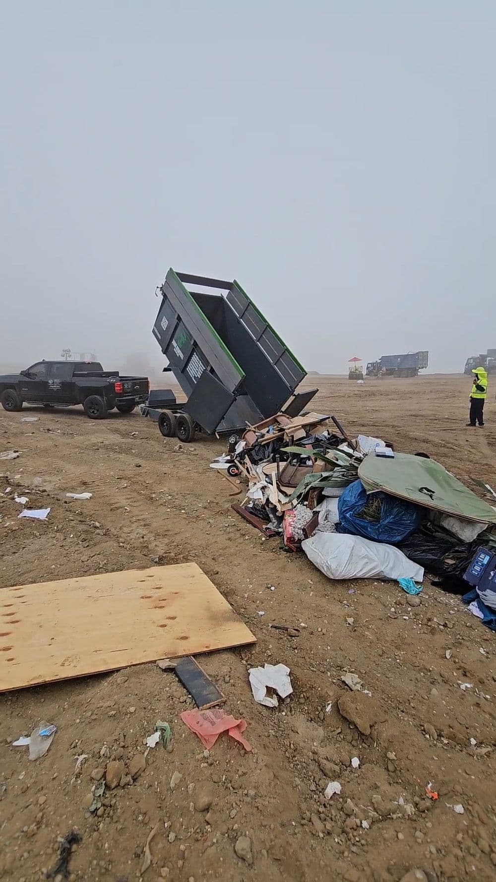 Dump truck unloading a green dumpster filled with debris at a construction site.