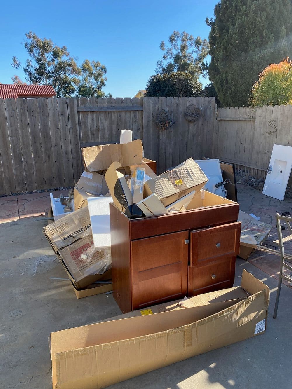 Wooden cabinet surrounded by cardboard boxes and trash in a backyard setting.