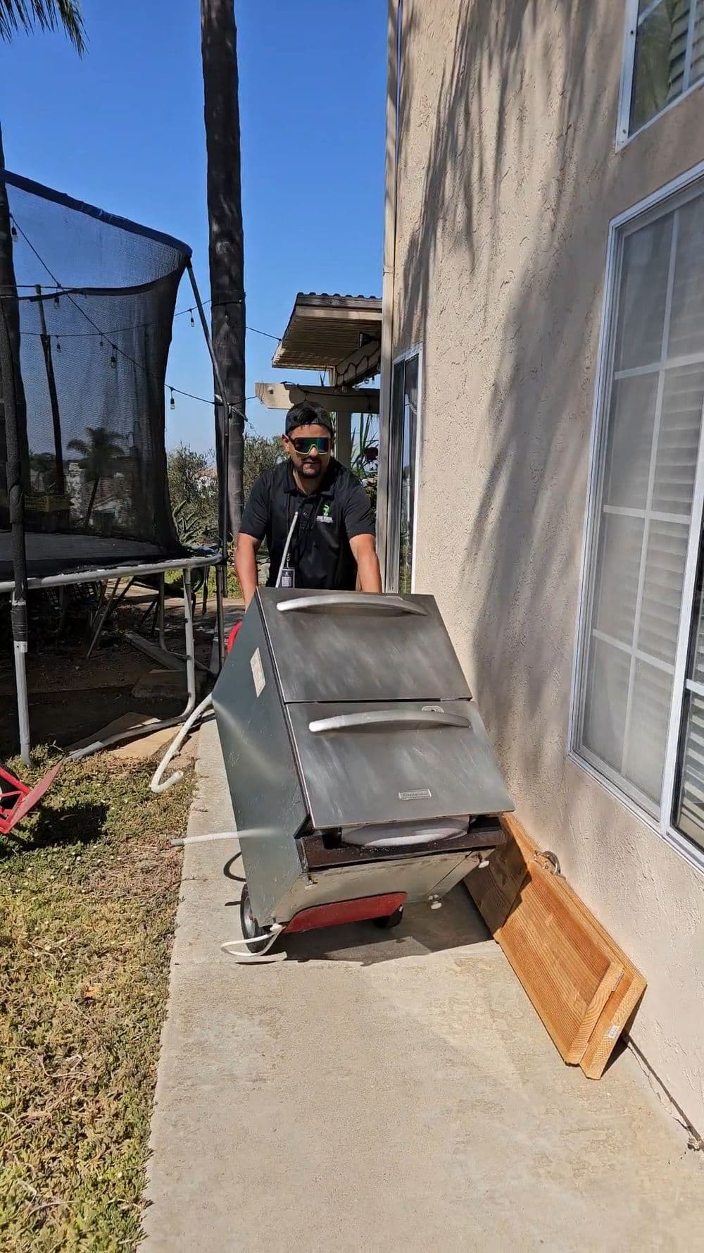 Man moving a stainless steel grill along a concrete path beside a house.