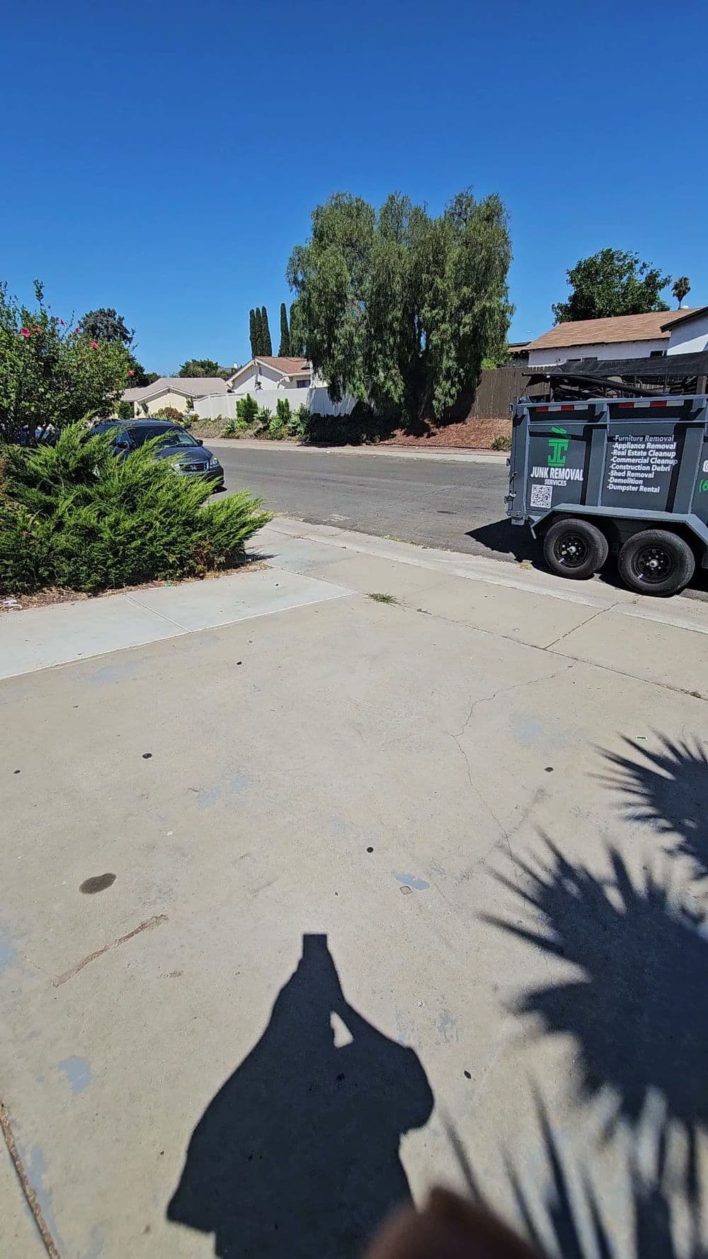 Street view with a dumpster on the curb, surrounded by houses and greenery.