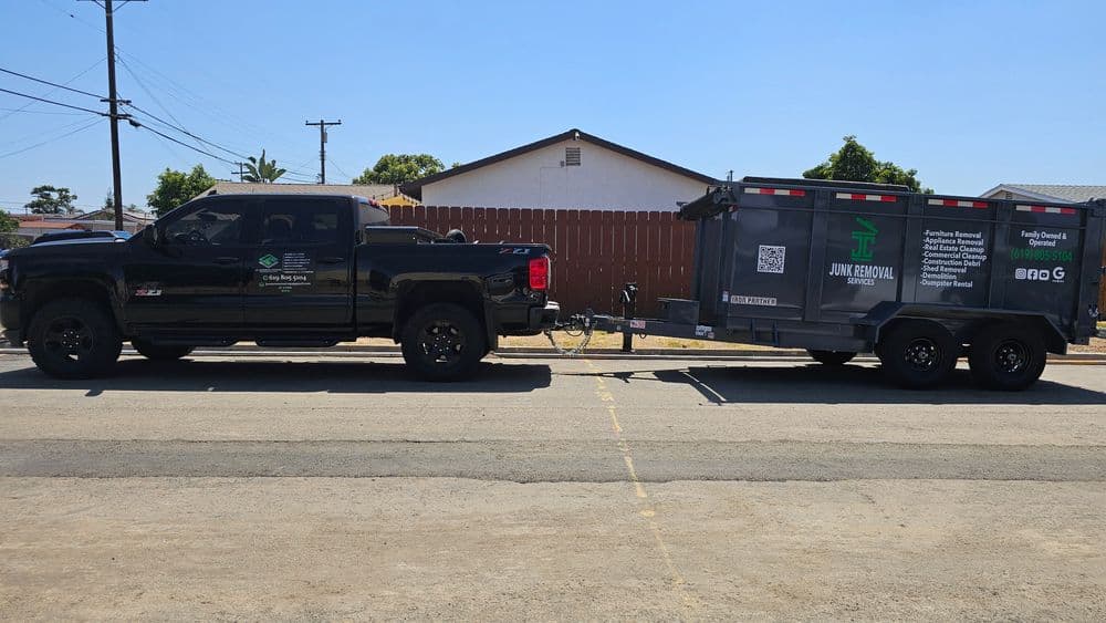 Black pickup truck towing a junk removal trailer on a residential street.