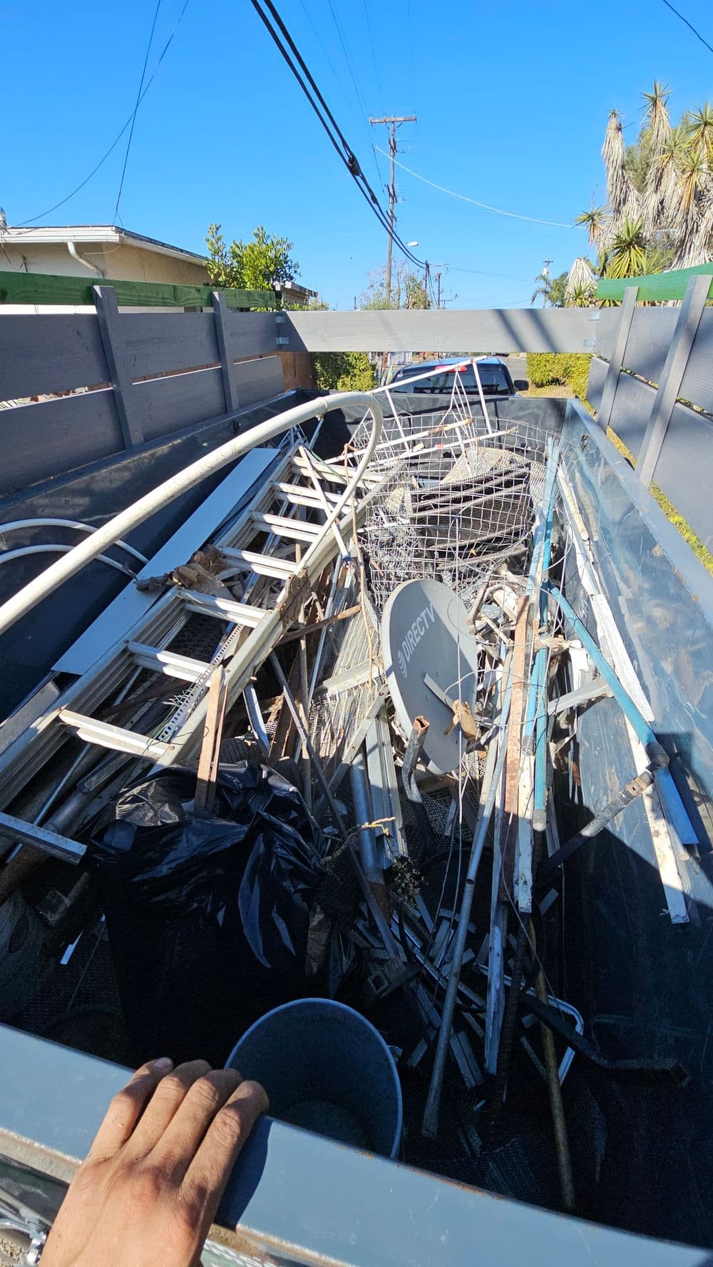Dump truck filled with debris, including metal pipes, a ladder, and plastic items.