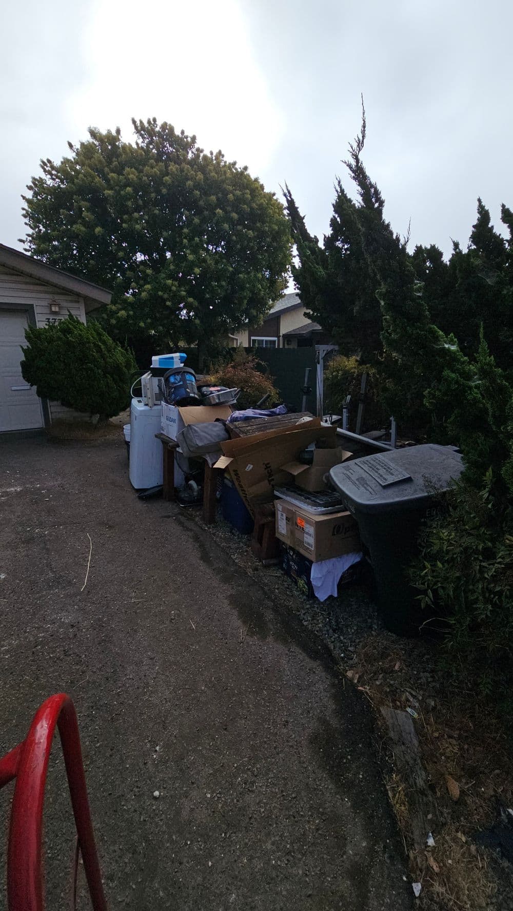 Cluttered driveway with boxes, appliances, and yard waste under cloudy skies.