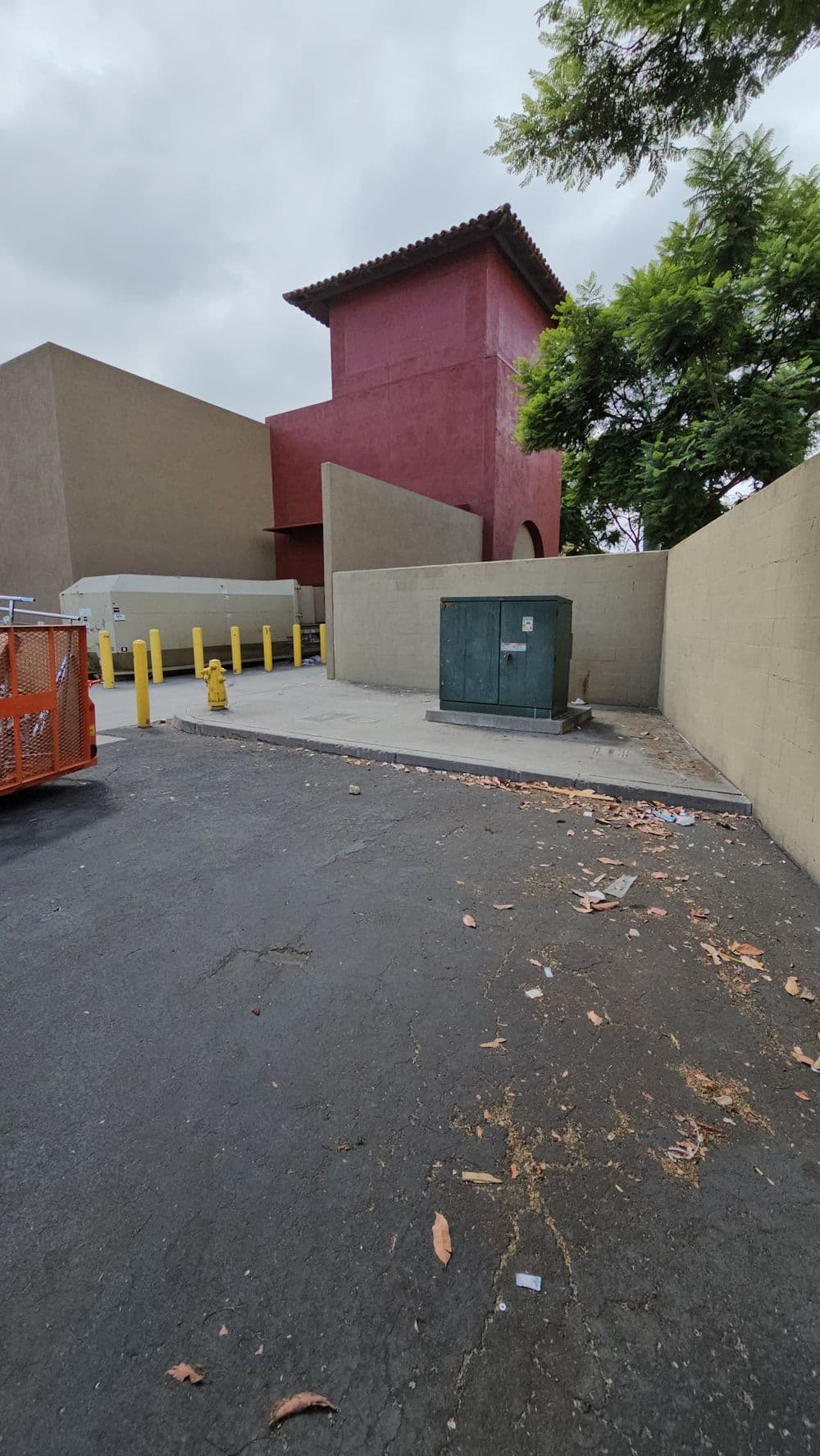 Exterior view of a building with a red accent wall, green utility box, and parking area.