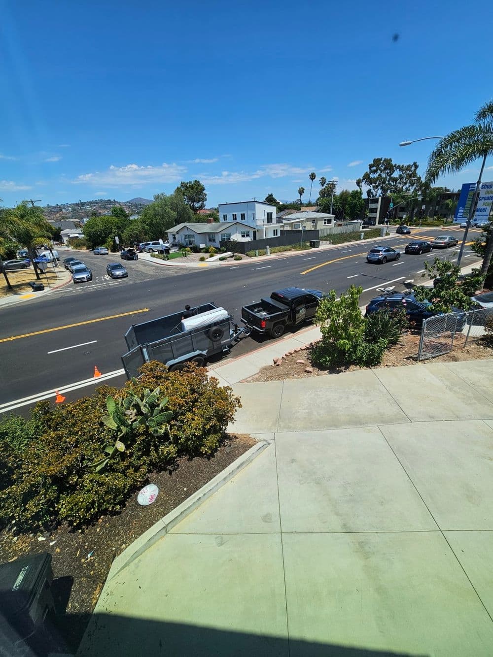 View of a busy street with cars, palm trees, and a trailer near residential buildings.
