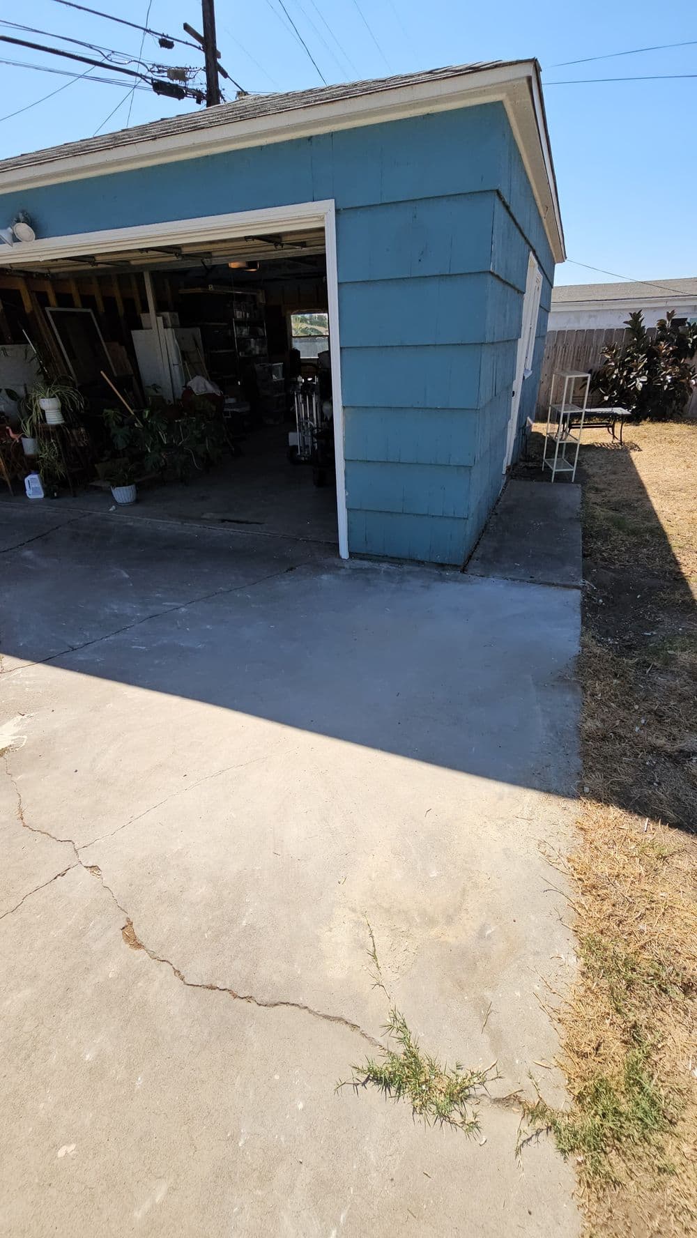Blue garage with concrete driveway, surrounded by dry grass and power lines in the background.