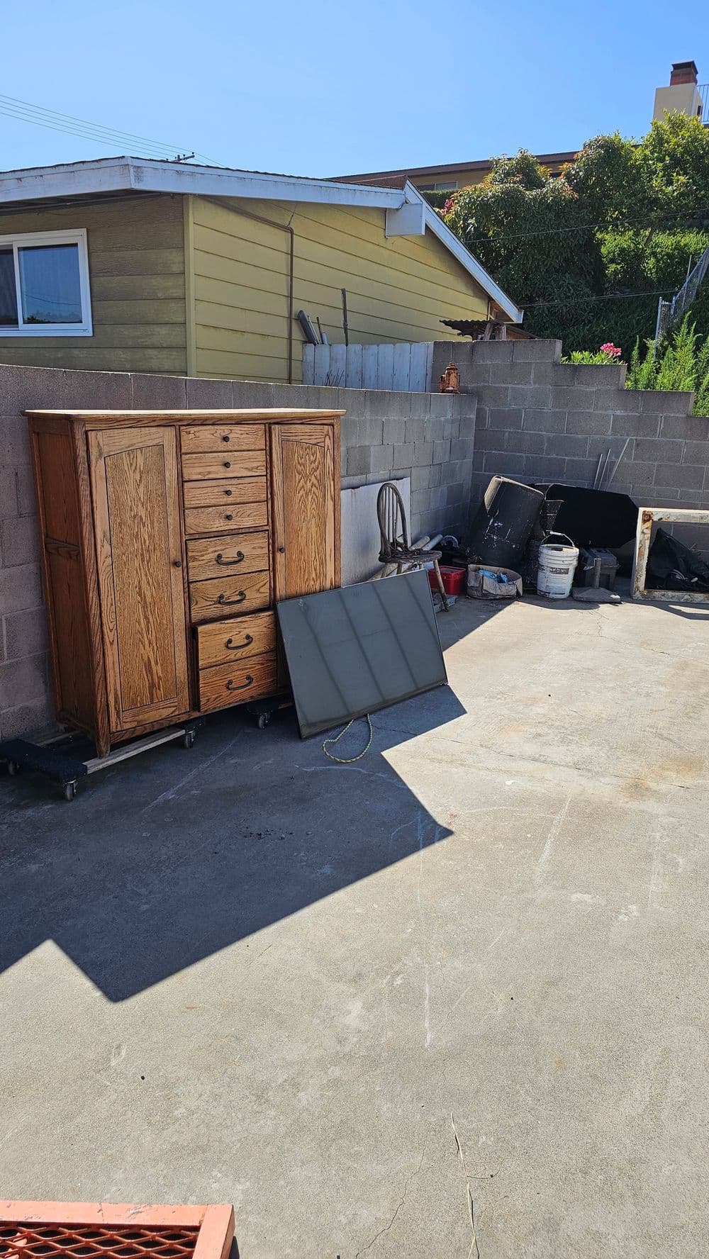 Outdoor storage area with a wooden cabinet, chair, and various tools on concrete surface.