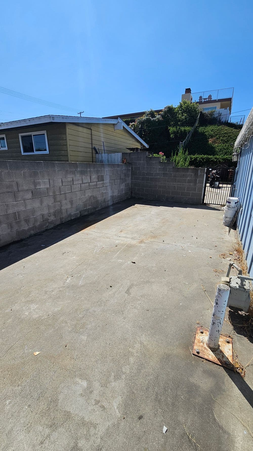 Empty concrete area beside a house, enclosed by a gray block wall and blue siding.