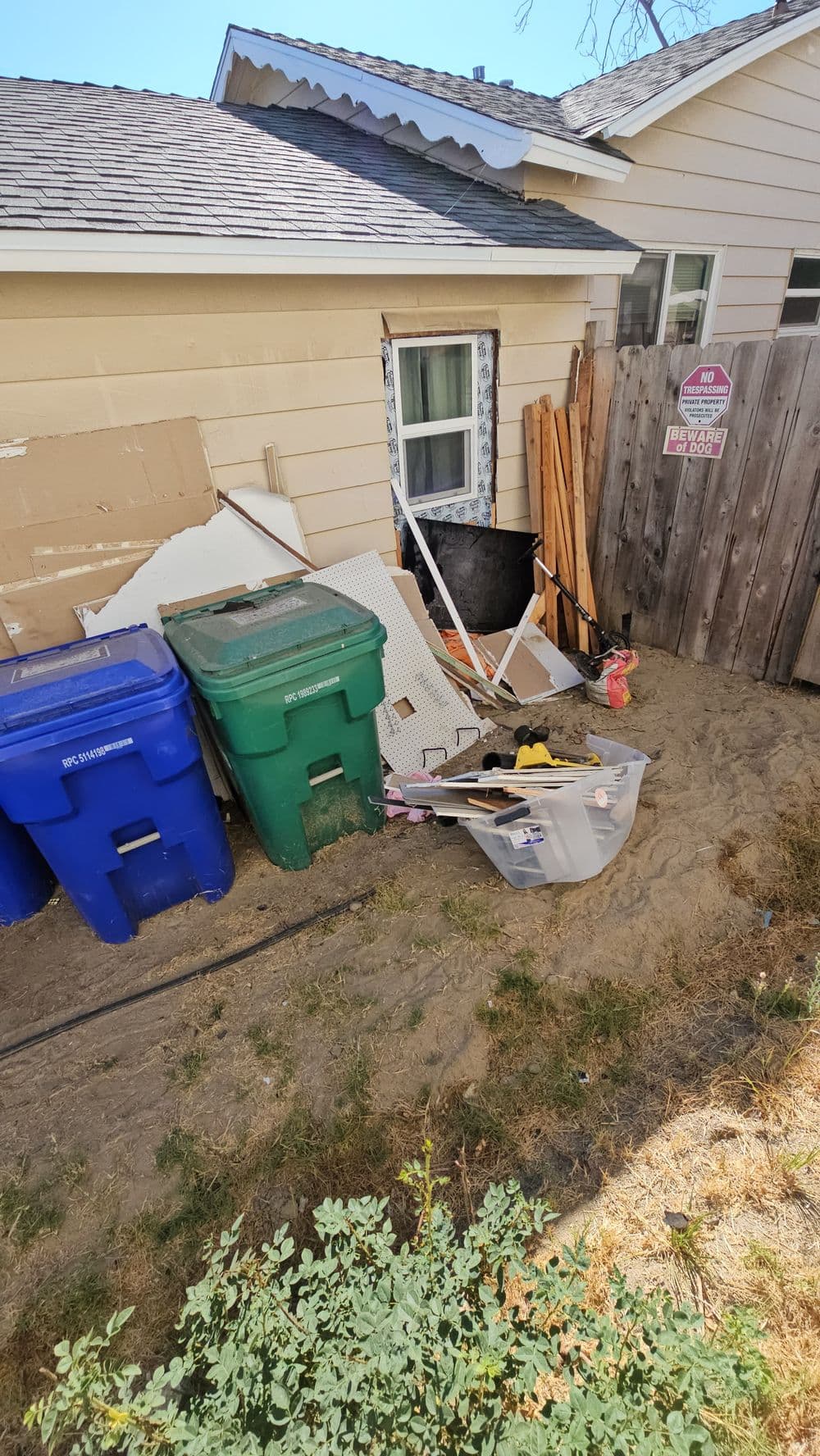 Cluttered backyard area with bins, debris, and construction materials near a house.