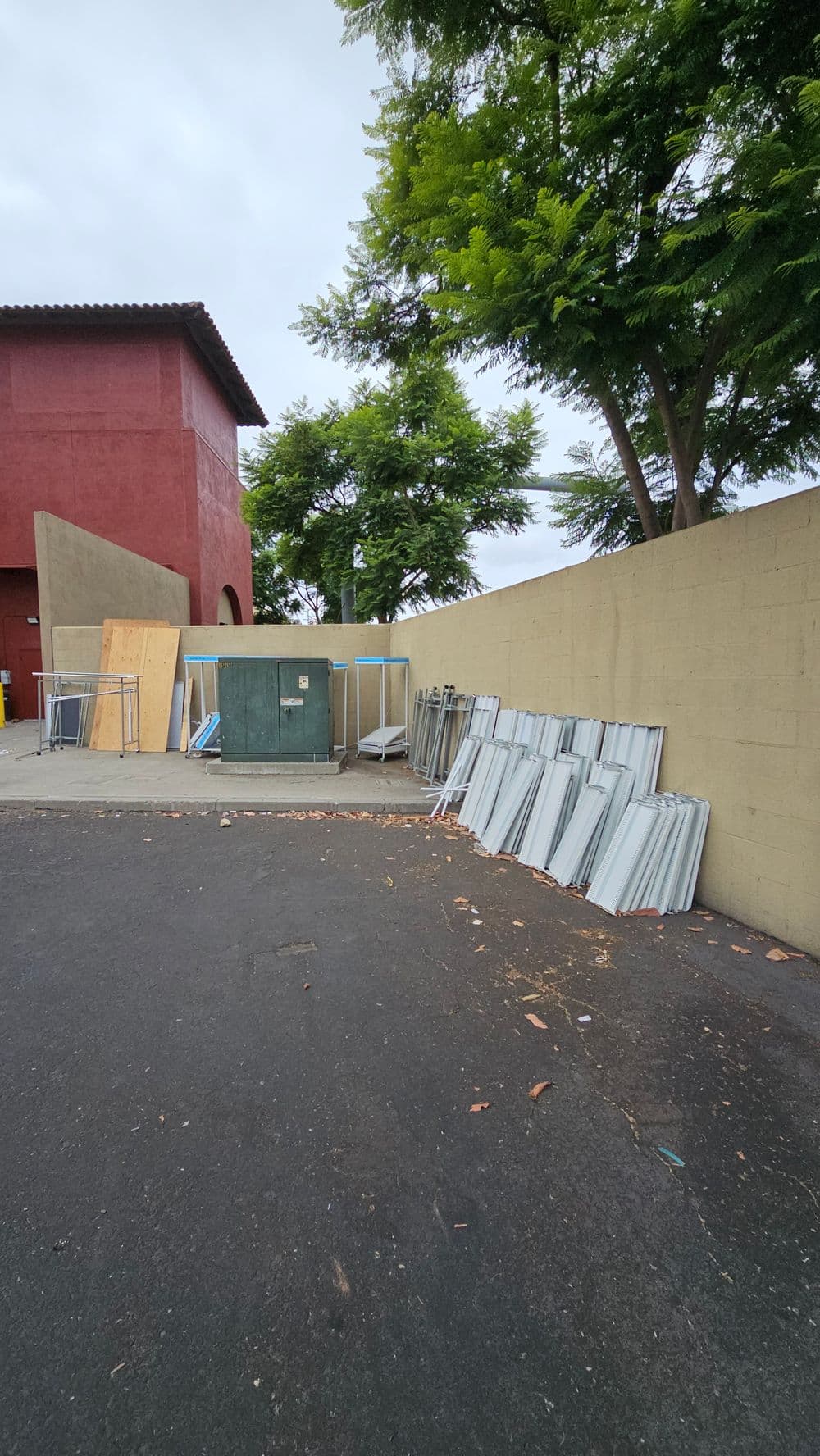 Storage area with stacked metal frames and a green dumpster, surrounded by trees.