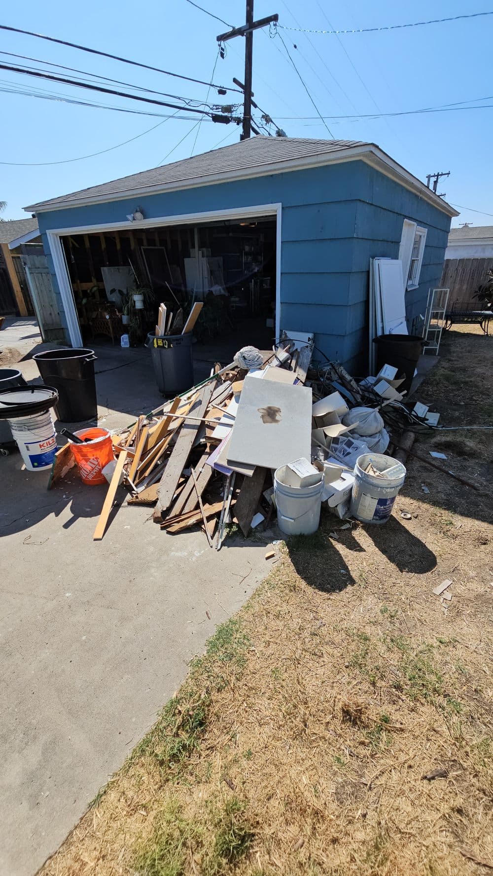 Piled debris and construction materials in front of a blue garage on a sunny day.