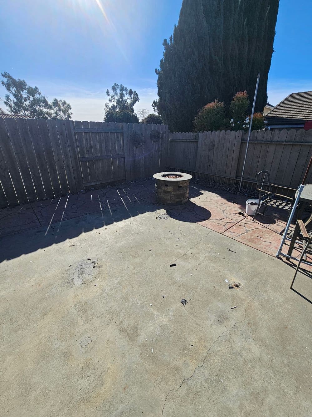 Empty backyard with a circular fire pit and walls of wooden fencing under a sunny sky.